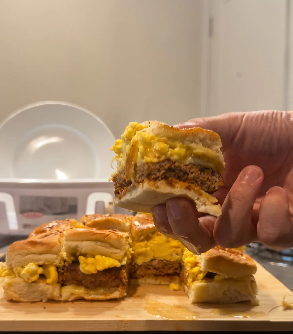 A BAHM breakfast slider lifted from the tray: turkey patty, scrambled eggs and melted pepper jack on a Hawaiian roll