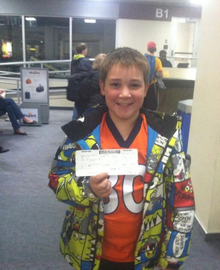 Alex in a Broncos jersey holding his boarding pass at the airport gate