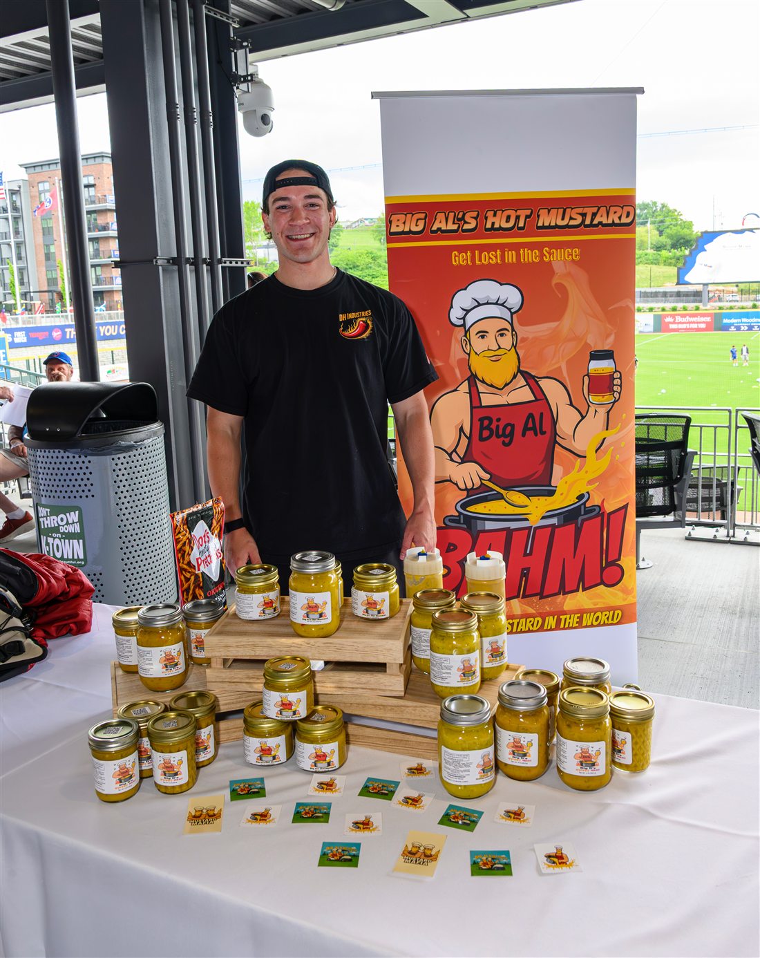 Alex smiling behind a table of Big Al's Hot Mustard jars in front of the Big Al banner