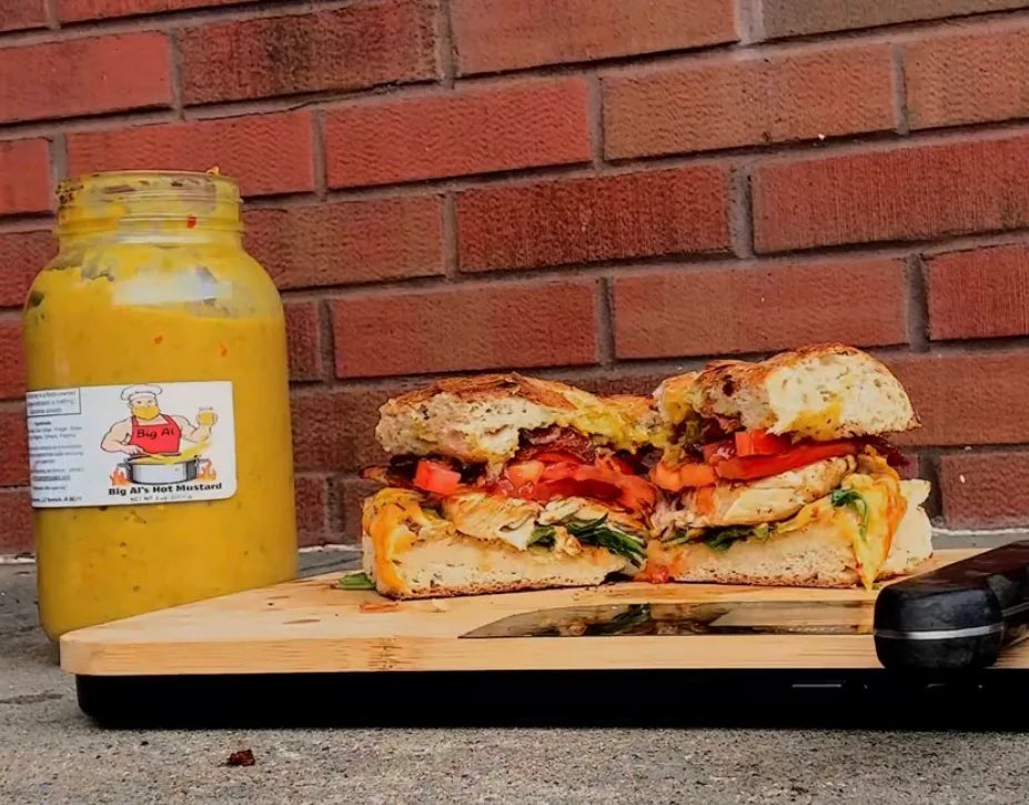 The BAHM Chicken Deluxe Sandwich from the reel, cut in half next to a jar of Big Al's Hot Mustard